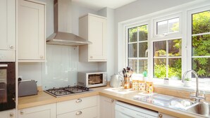 Une cuisine moderne avec des meubles blancs, une cuisinière à gaz, un four encastré et une fenêtre donnant sur un paysage verdoyant.