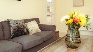 Un salon avec un canapé gris, un vase rempli de fleurs jaunes et une table basse en bois.