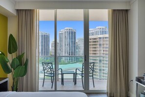 A hotel room with a large sliding glass door leading to a balcony with a view of high-rise buildings.