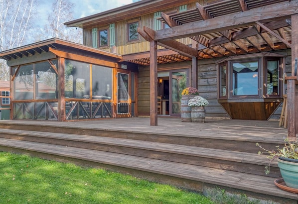 Une cabane en bois dotée d’une terrasse couverte, de grandes fenêtres et d’une cheminée en pierre.
