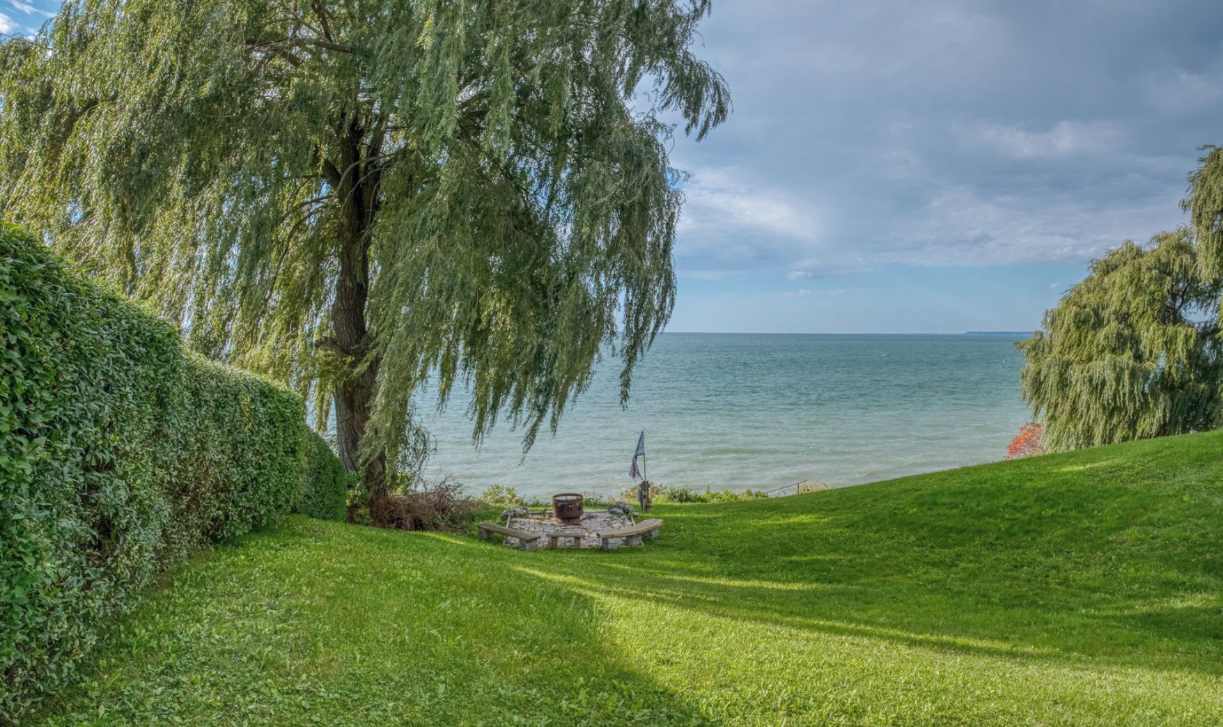 Une vue paisible sur le lac, avec une pelouse bien entretenue, un foyer en pierre et un grand saule.