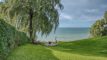 Une vue paisible sur le lac, avec une pelouse bien entretenue, un foyer en pierre et un grand saule.