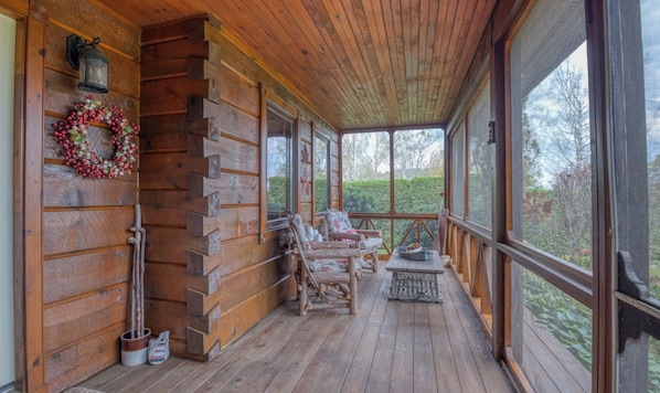 Una cabaña de troncos con un porche, paredes de madera, una corona, una silla y una mesa.
