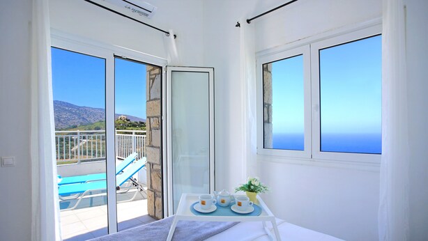 A room with a bed, a table with cups and a plant, and a view of a pool and mountains. - Villa With 180 Degree Sea View - Sleeps 2-6 (Malevizi)