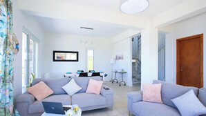 A modern living room with two sofas, a coffee table, and a laptop. There is a dining area in the background with a table and chairs. - Villa With 180 Degree Sea View - Sleeps 2-6 (Malevizi)