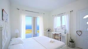 A bedroom with a bed, a bedside table, a fan, a potted plant, and a view of the sea. - Villa With 180 Degree Sea View - Sleeps 2-6 (Malevizi)