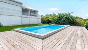 A rectangular swimming pool with a wooden deck, surrounded by a white building with a balcony.