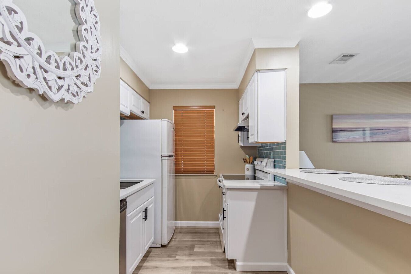 A compact kitchen with white cabinetry, a built-in oven, and a window with blinds.