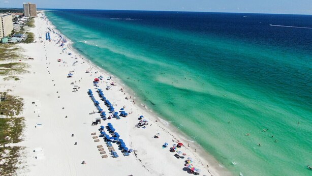 Een strand met helder turquoise water, een lange strook wit zand en een rij blauwe parasols.