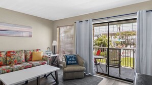 Een woonkamer met een bank, een tafeltje en een stoel. Er is een balkon met uitzicht op de omgeving.