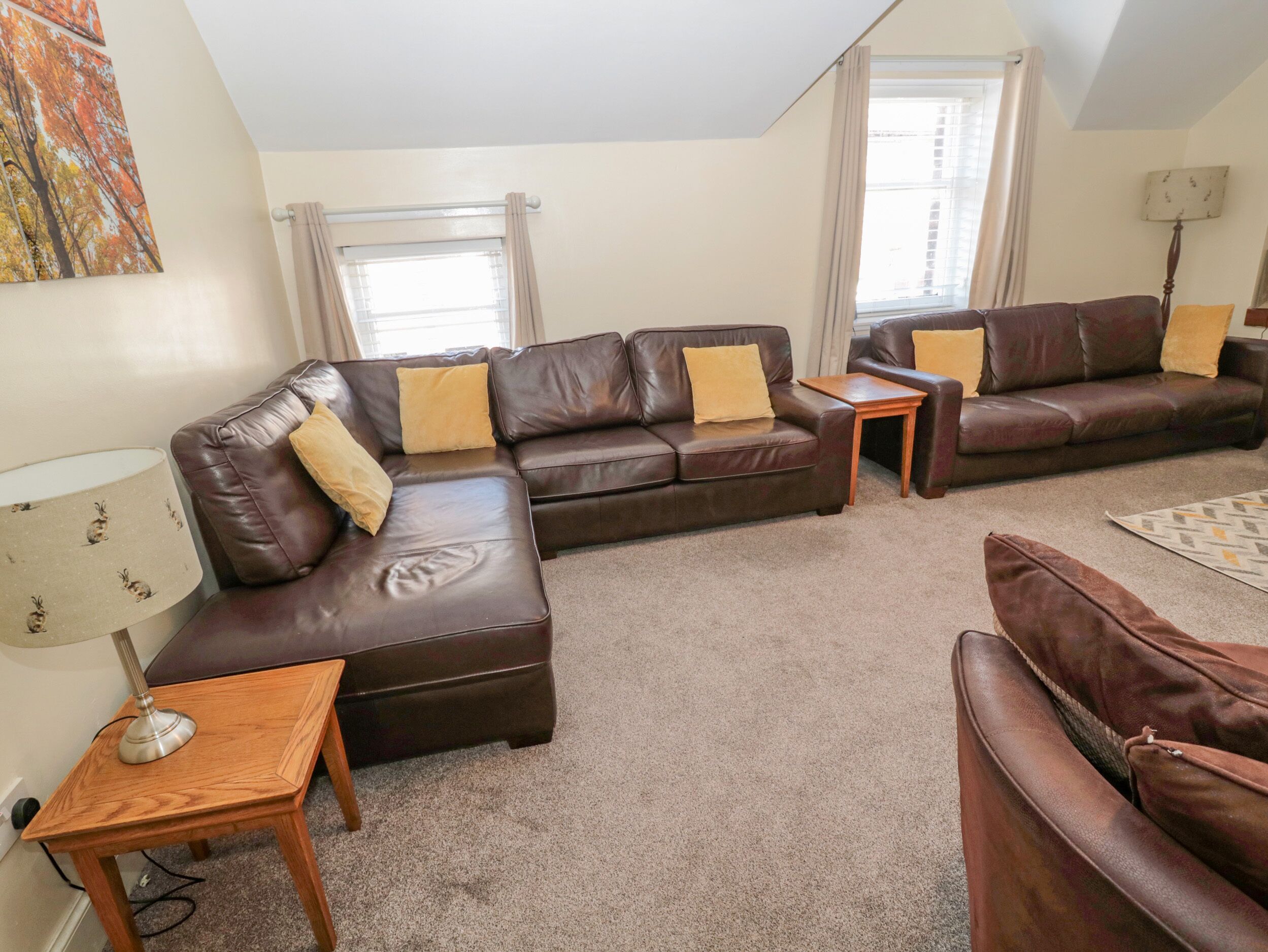 A living room with a brown leather sofa, a wooden side table, and a lamp.