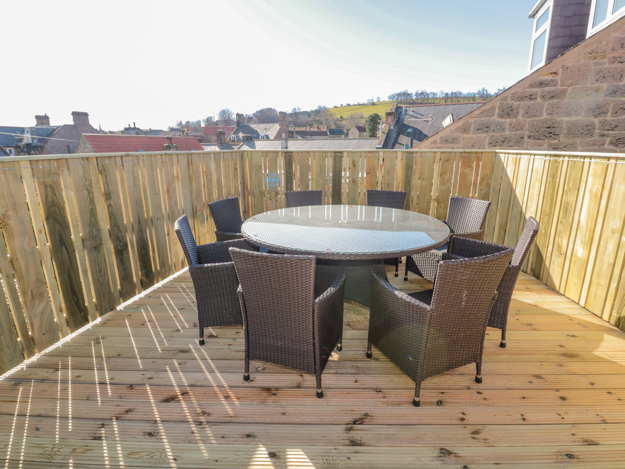 Una terraza de madera con una mesa redonda y sillas, rodeada por una valla de madera.