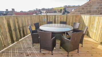 Una terraza de madera con una mesa redonda y sillas, rodeada por una valla de madera.