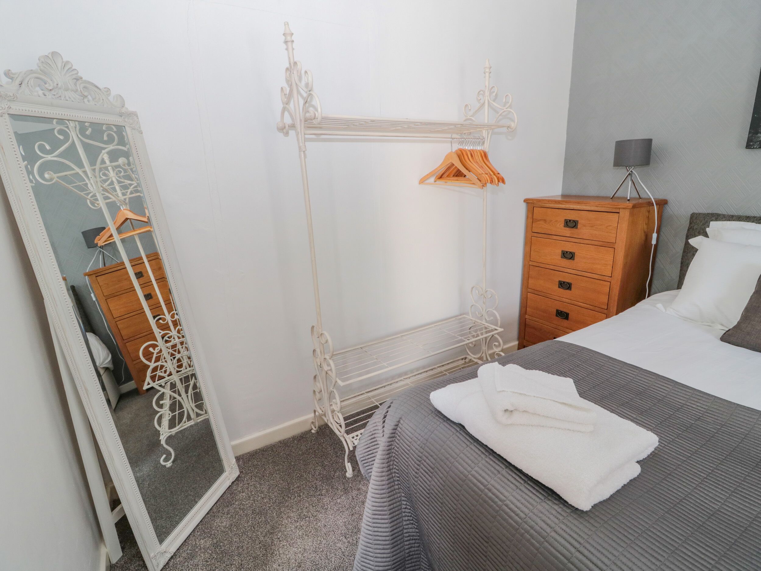 Un dormitorio con cama, cómoda, espejo y armario metálico con perchas.