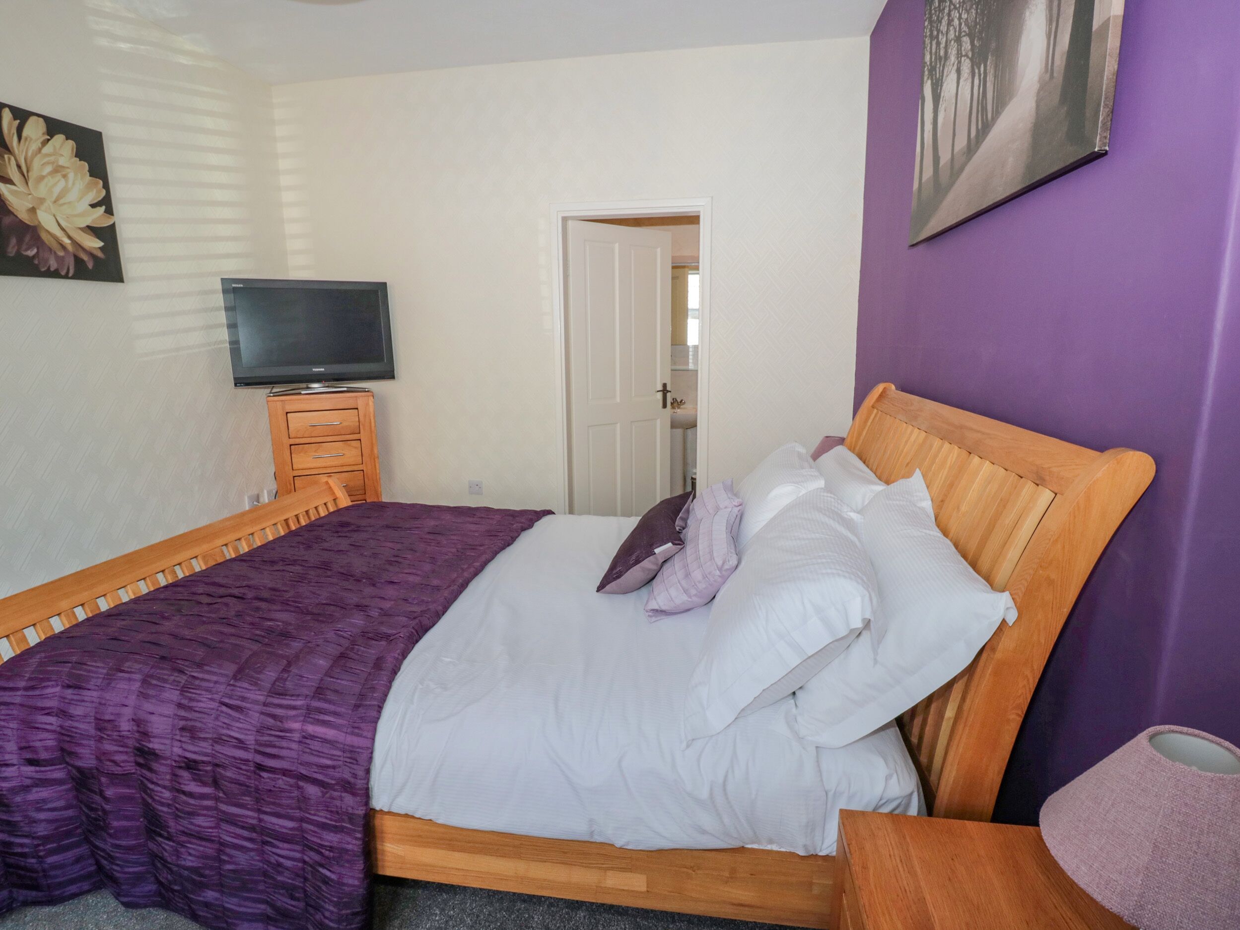 Een slaapkamer met een bed, een televisie op een houten dressoir, en een deur naar een badkamer.