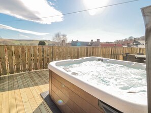 Et boblebad på en træterrasse med udsigt over et landligt landskab og huse i baggrunden.