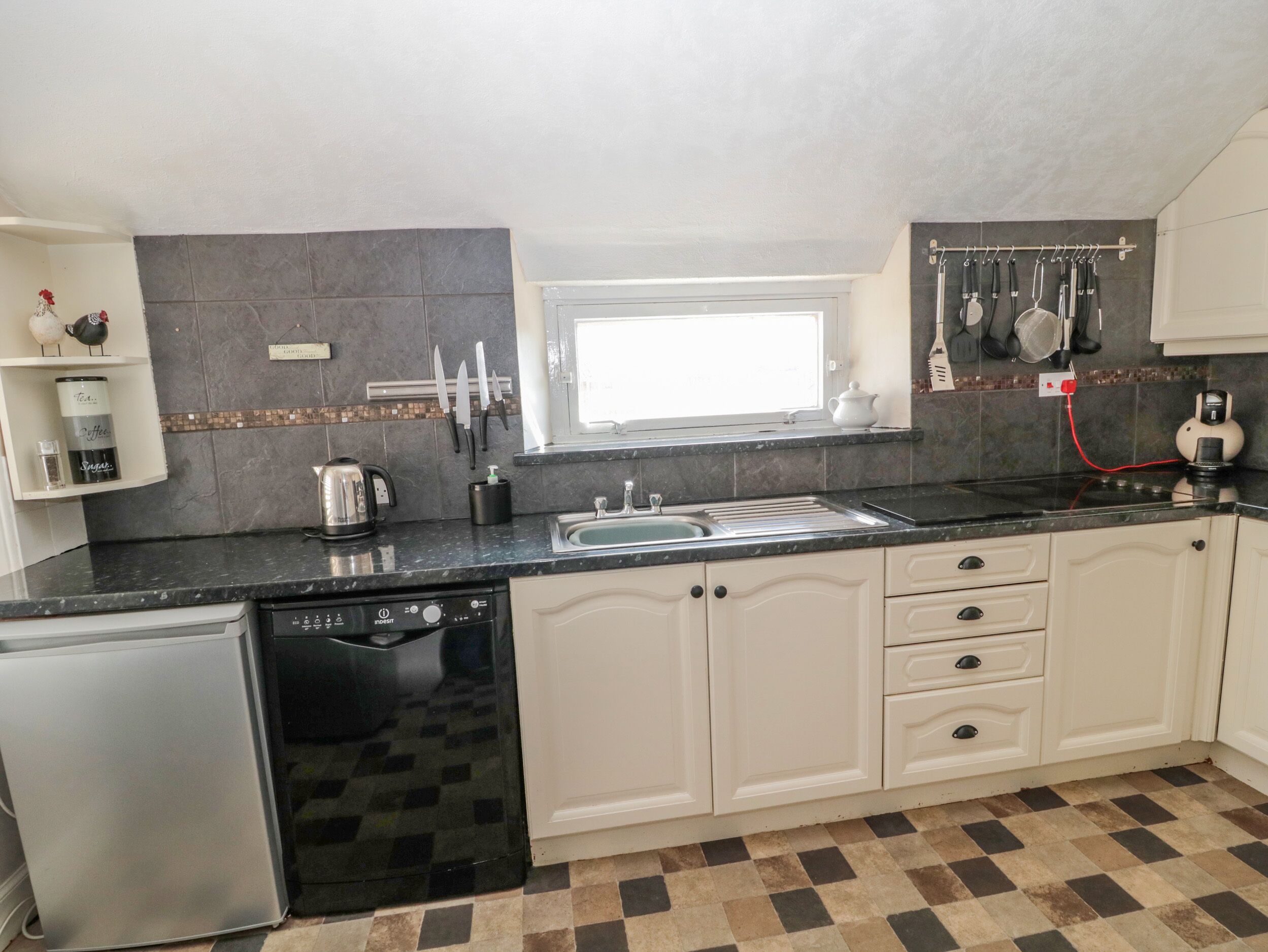 A kitchen with a dishwasher, a sink, and a window above it. There are cabinets and a countertop.