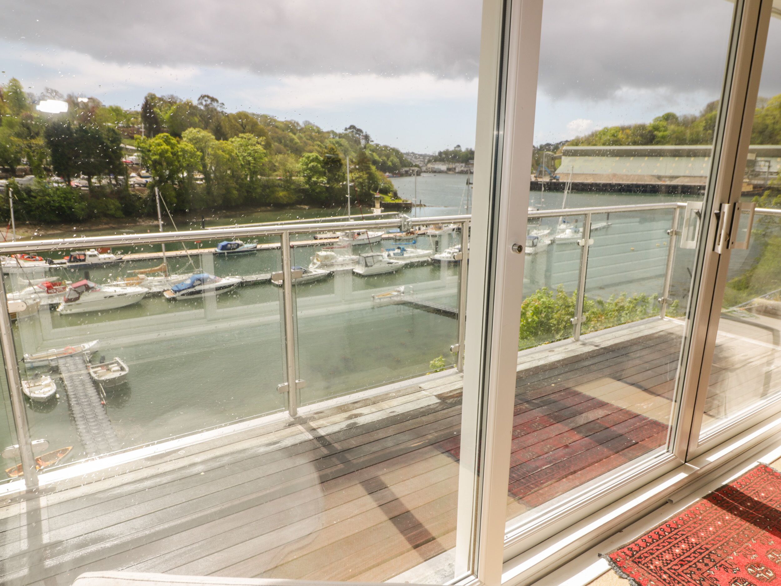 A view from a balcony overlooking a marina with boats docked, a river, and a cloudy sky.