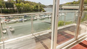 Une vue depuis un balcon donnant sur une marina où sont amarrés des bateaux, sur une rivière et sur un ciel nuageux.