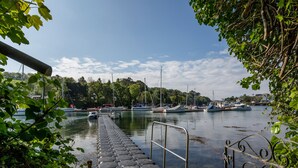 Une jetée menant à un port tranquille, où l’on peut voir des bateaux et de la végétation.
