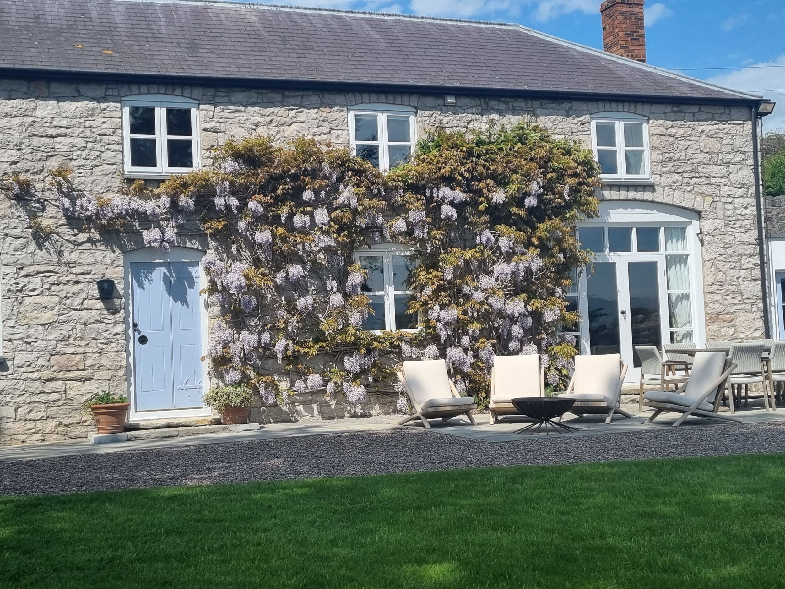 A stone house with a white door, two windows, and a covered patio with outdoor furniture.