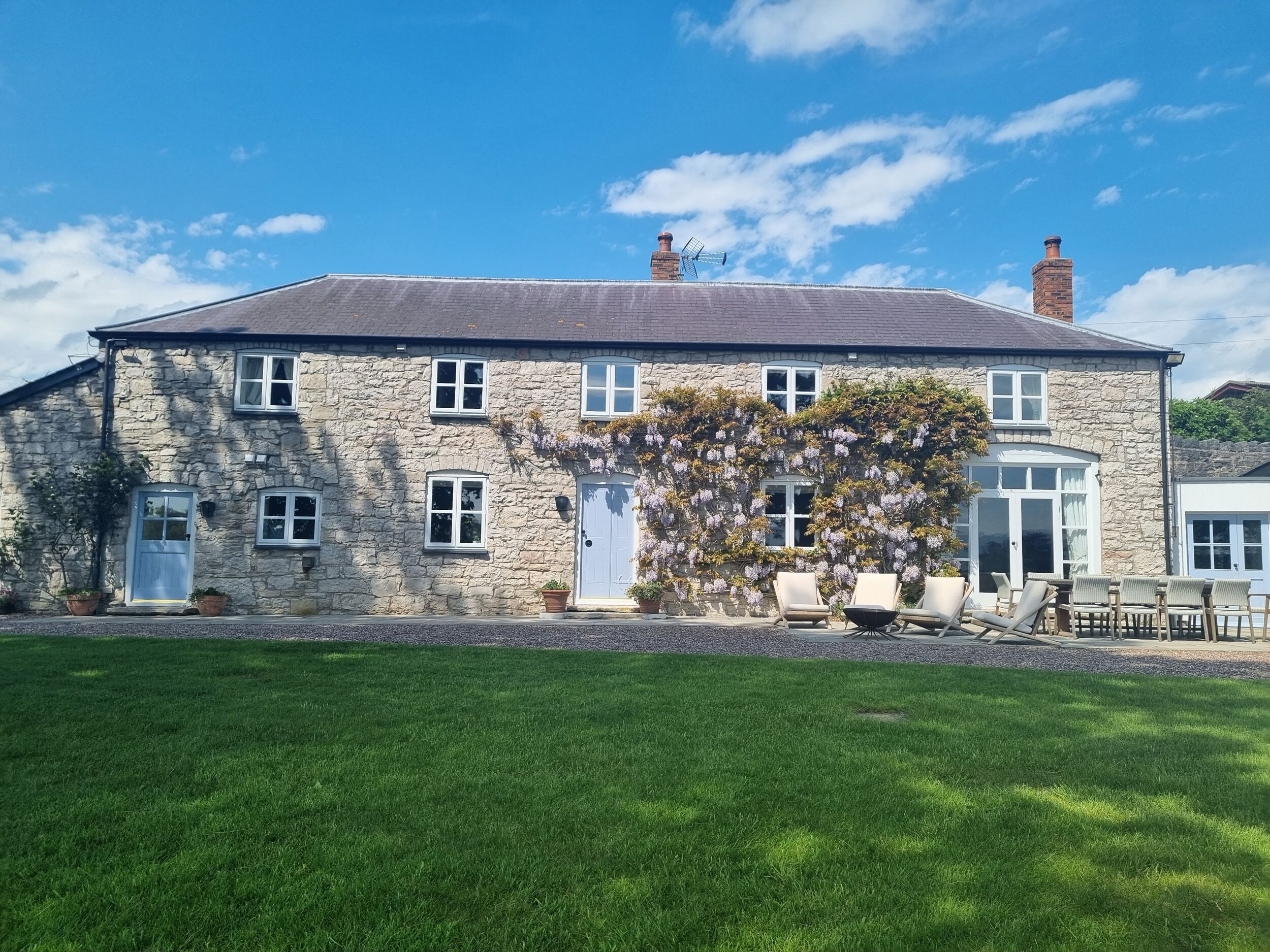 A stone building with a flat roof, multiple windows, and a door. There is a garden with grass in front.