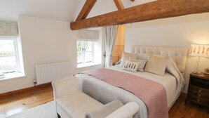 Un dormitorio con una cama grande, techo de madera, ventana con cortinas, un radiador y una mesita de noche con lámpara.