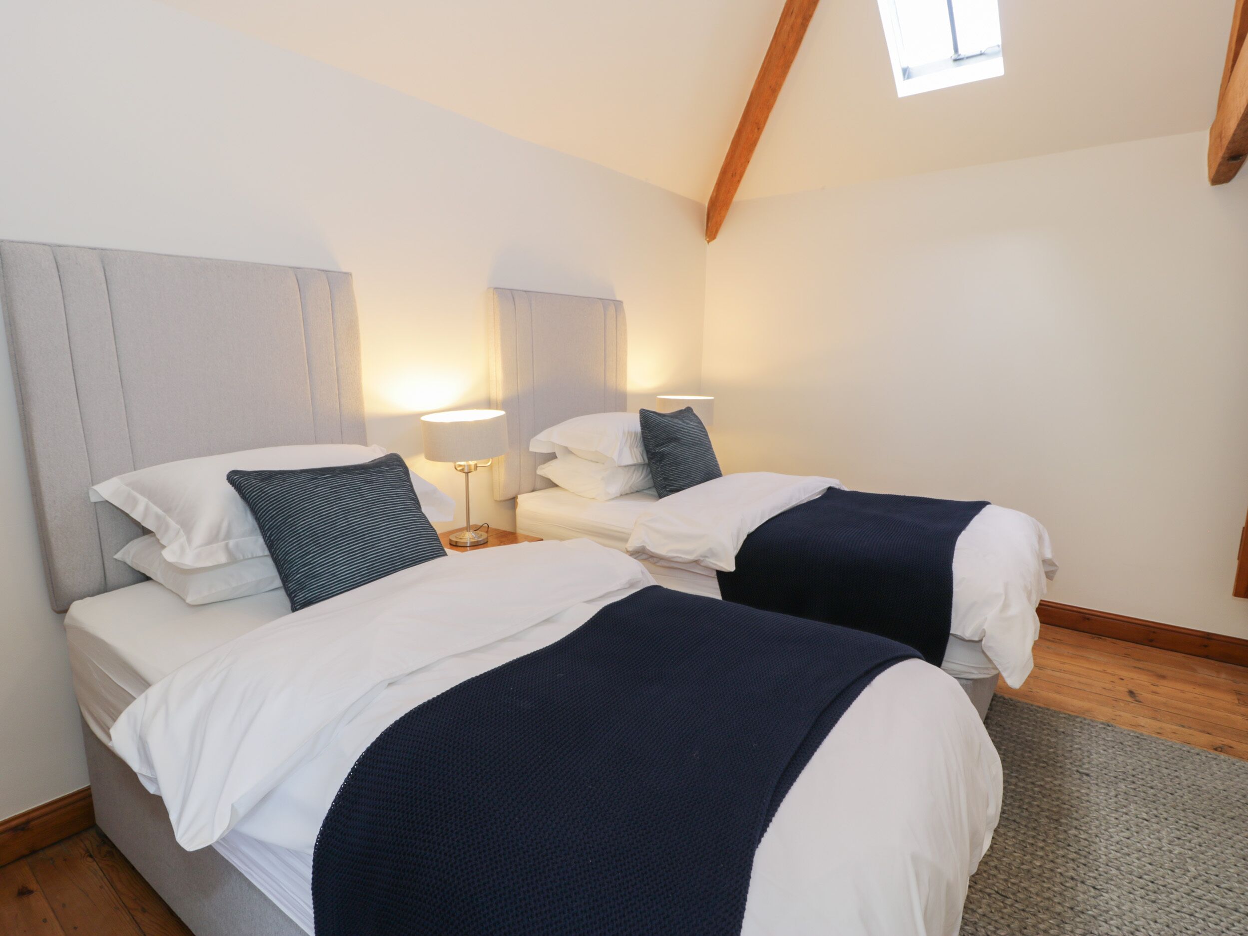Une chambre d’hôtel avec deux lits, une poutre en bois au plafond et une fenêtre laissant entrer la lumière naturelle.