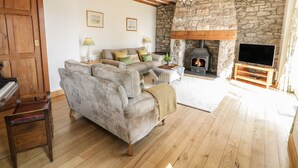 Una sala de estar acogedora con chimenea de piedra, vigas de madera, un sofá, un piano y un televisor.