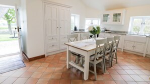 Una cocina amplia con armarios blancos, una mesa de comedor con sillas y un ventanal que proporciona luz natural.