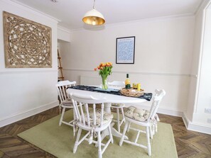Een eethoek met een witte tafel, vier stoelen, een bloevas, een lijstwerk en een hanglamp.