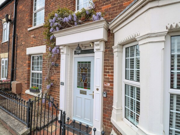 A traditional brick house with a white front door, a small window with a decorative grille, and a black metal gate.