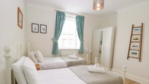 A twin bedroom with two beds, a window with curtains, a fan, and a wardrobe. - Springfield (Fakenham)