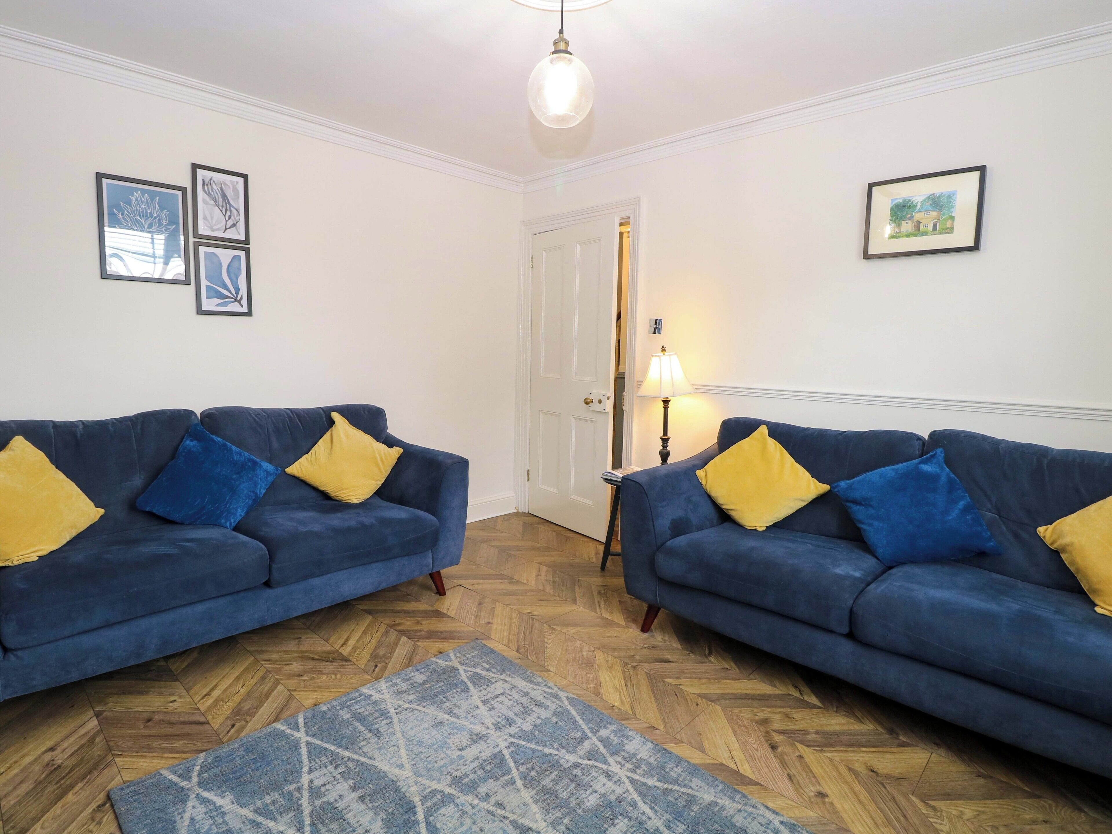 A room with two blue sofas, a patterned rug, and framed artwork on the walls.