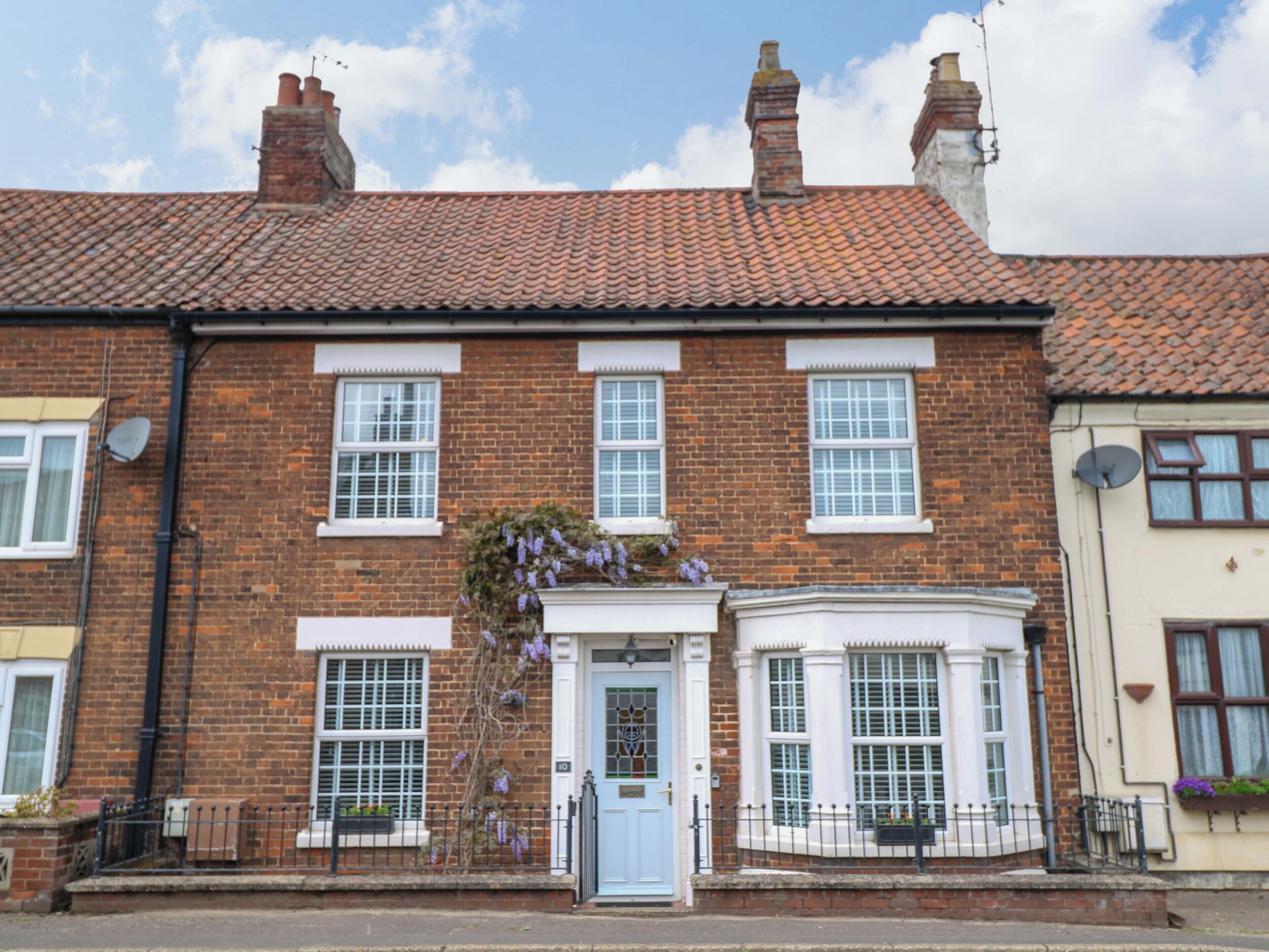 A two-story brick house with a red-tiled roof, white-framed windows, and a blue door.