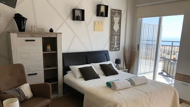 A hotel room with a bed, a desk, a chair, a TV, and a balcony with a view.
