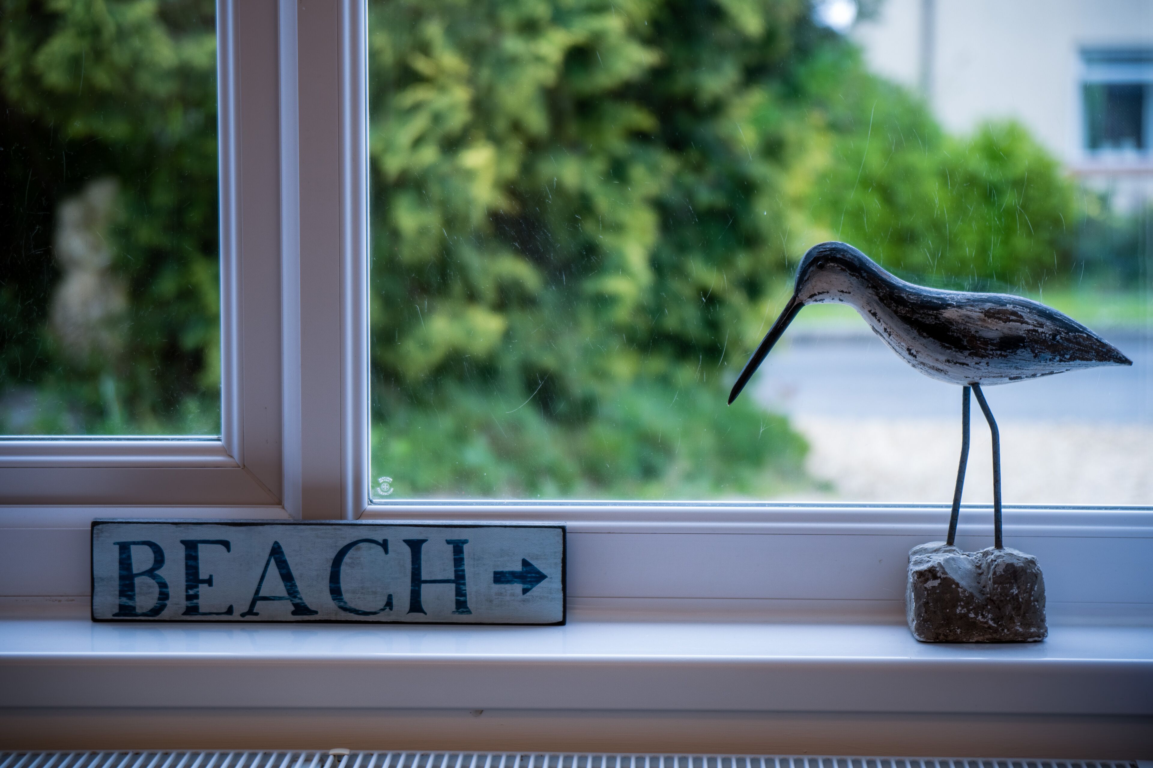 A bird figurine on a windowsill with a 'BEACH' sign below it.