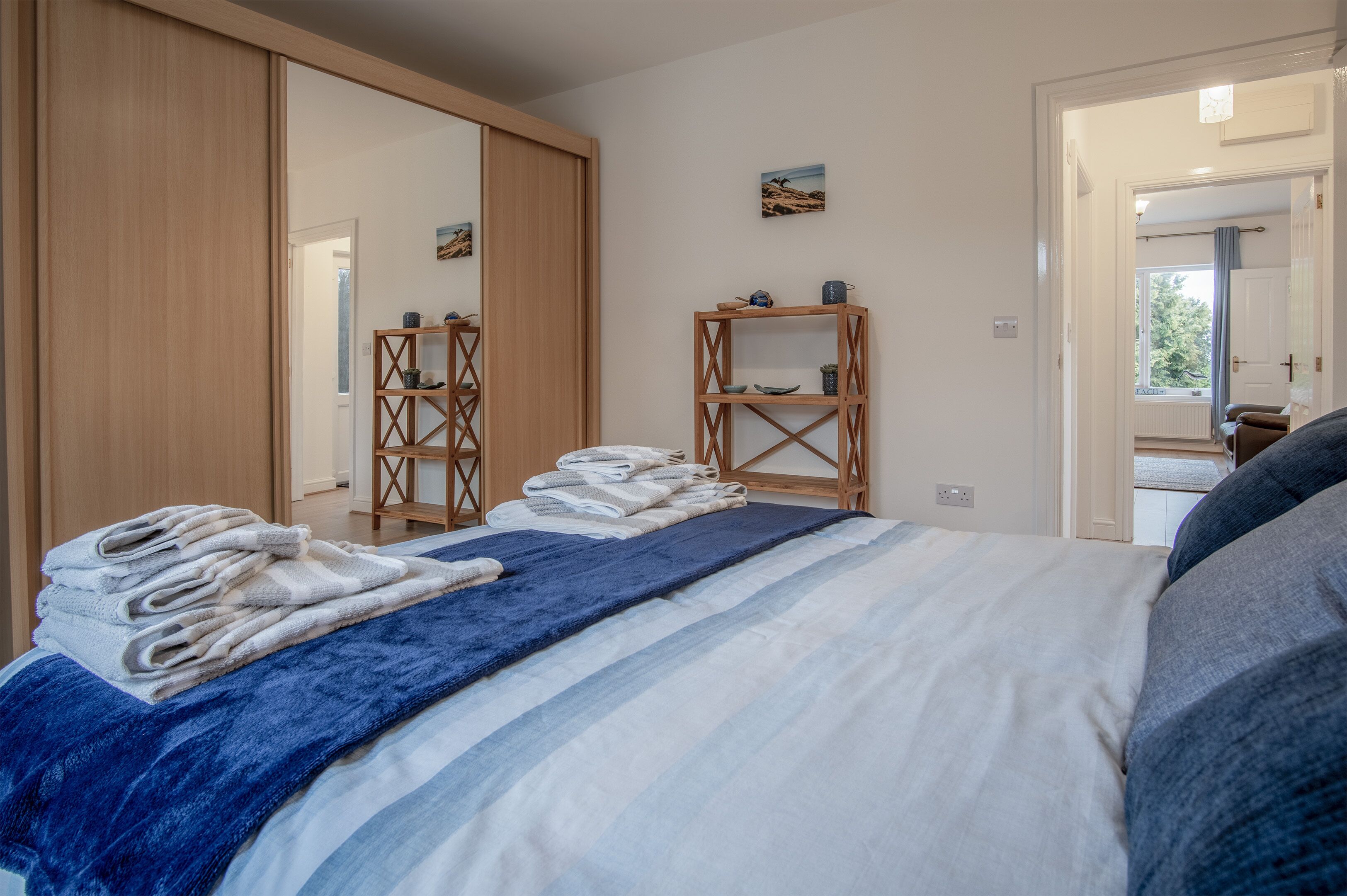 Ein Schlafzimmer mit einem Bett, einem Kleiderschrank, einem Regal mit Dekoration und Blick ins Freie.