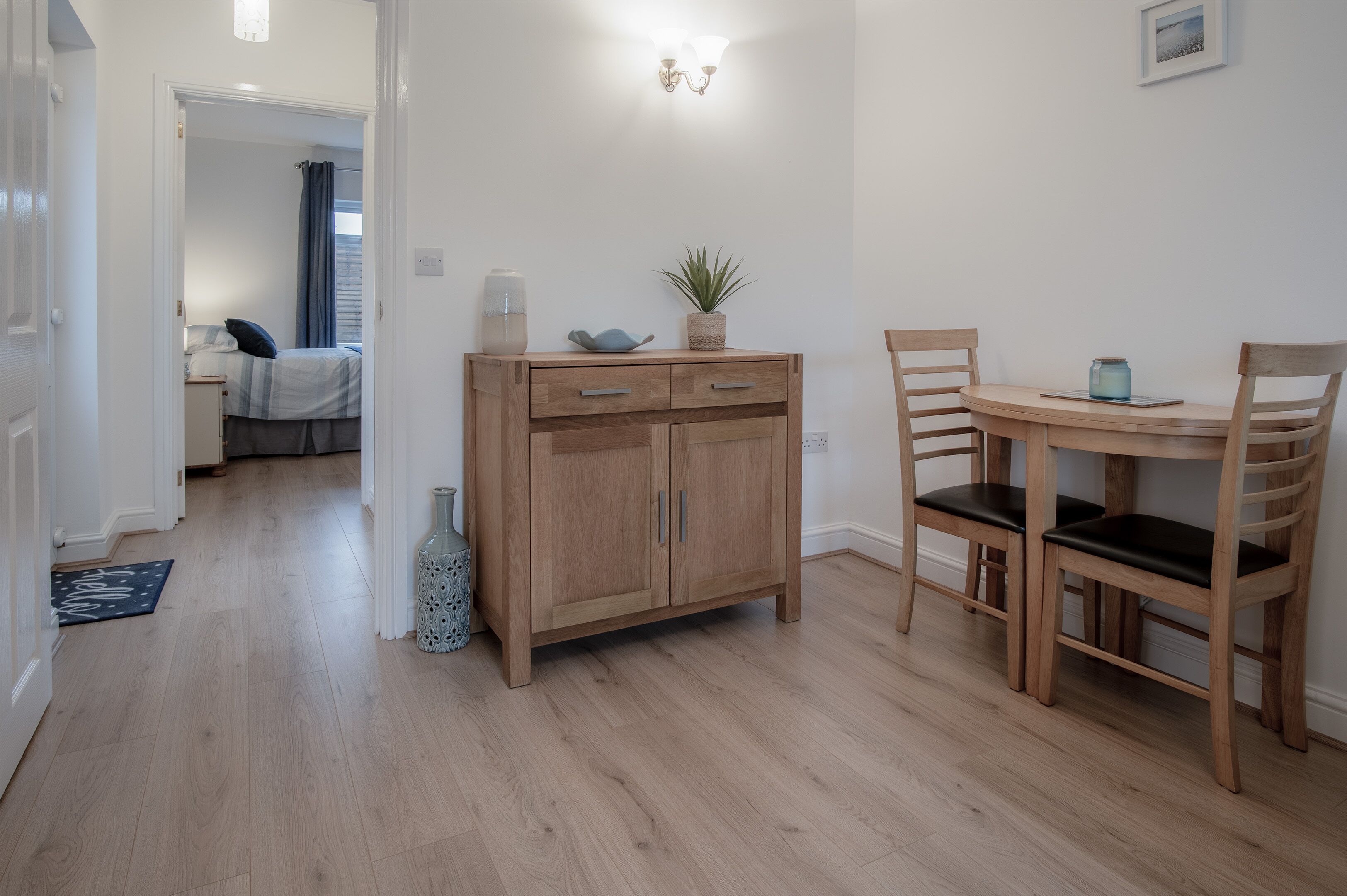 Una habitación con un armario de madera, una mesa de comedor con dos sillas y una cama al fondo.