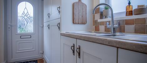 A kitchen with white cabinets, a sink, a wooden cutting board, and a window with frosted glass.