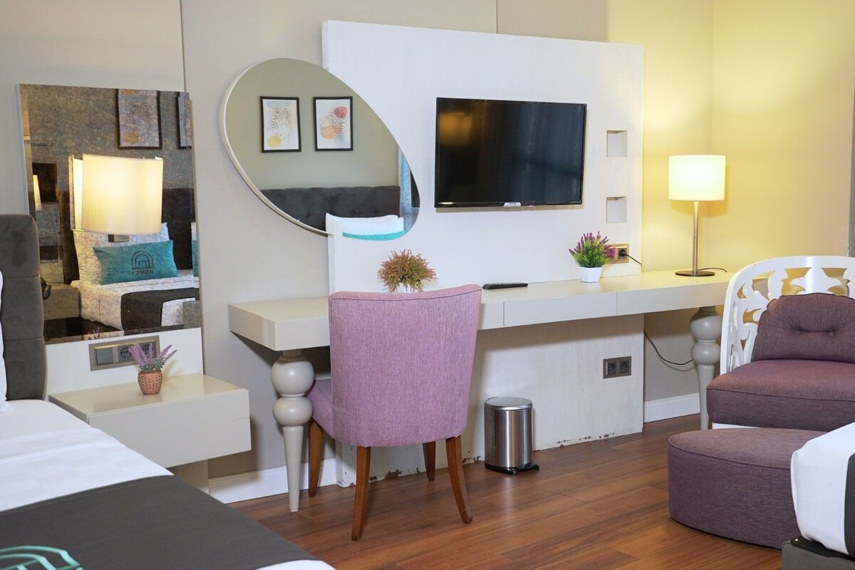 Habitación de hotel con cama, escritorio, silla, televisor, lámpara y cubo de basura.