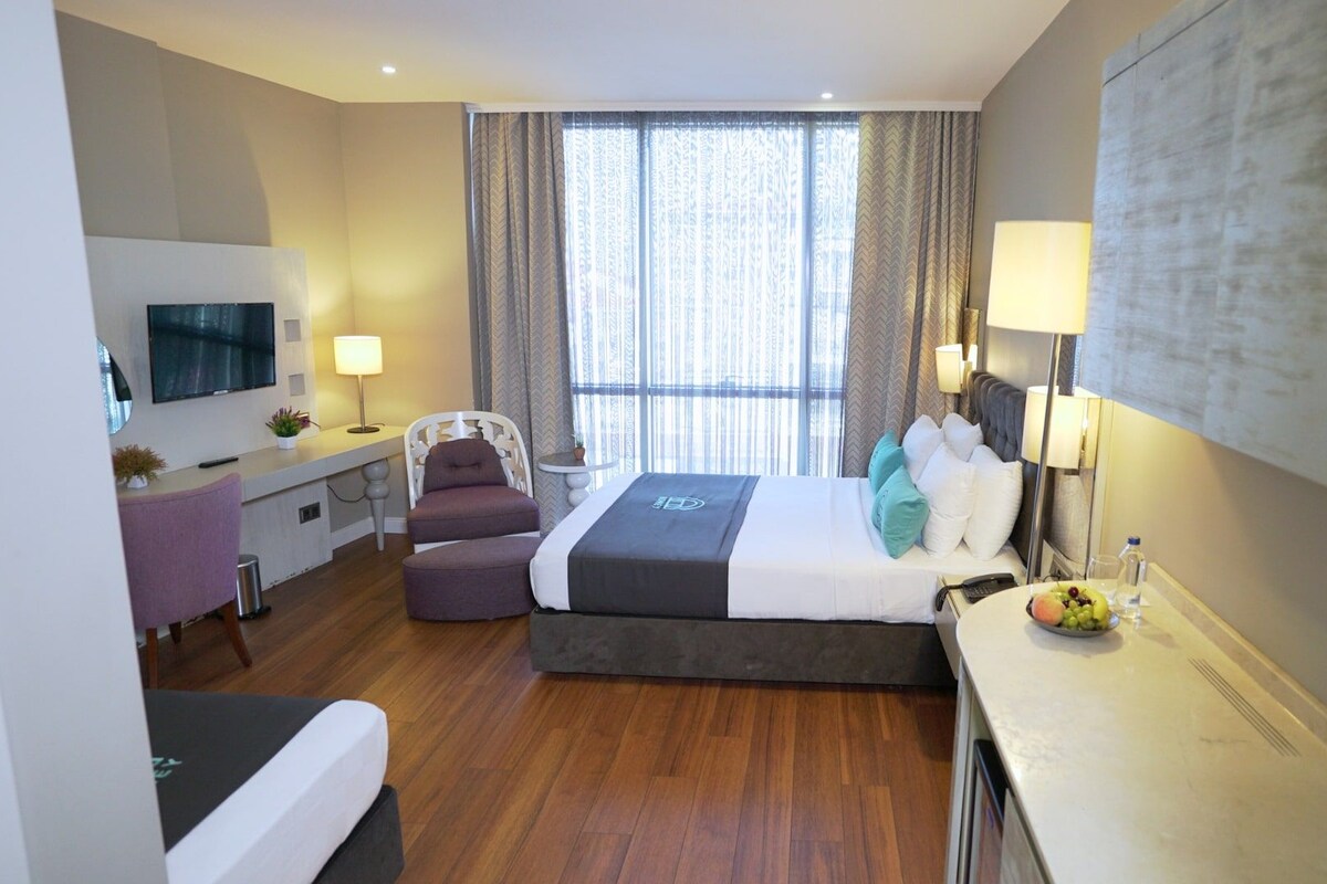 A hotel room with a bed, desk, chair, TV, and a view of the outdoors.