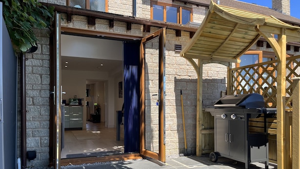 A house with a stone facade, a wooden pergola, and a barbecue grill.
