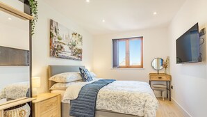 A modern bedroom with a bed, bedside tables, a mirror, and a window with a view.