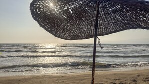 A beach umbrella with a woven design, positioned on a sandy beach with the ocean in the background. - Ephesus Retreat (Selçuk)
