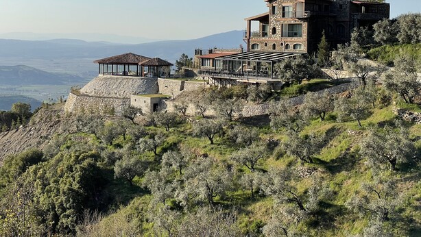 A large, stone building with multiple levels and a tower, surrounded by olive trees and hills. - Ephesus Retreat (Selçuk)