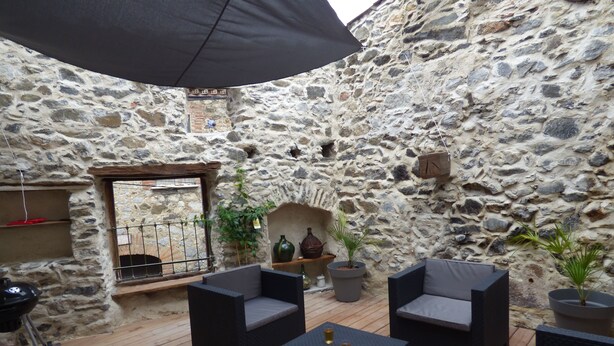 Une terrasse extérieure avec des murs en pierre, des meubles en osier et des plantes en pot.