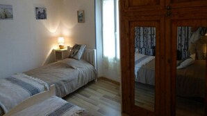 Une chambre avec deux lits simples, une table de chevet avec une lampe, une armoire en bois et une porte donnant sur une autre pièce.