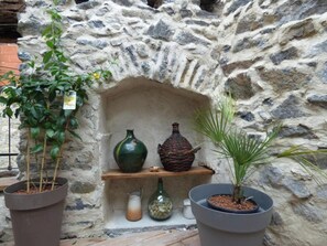 Una pared de piedra con una repisa que sostiene un jarrón verde, una maceta marrón y una planta pequeña.