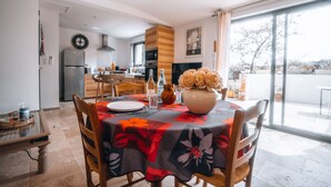 A dining area with a table set for two, a vase with flowers, and a kitchen in the background. - Le Titibu: Gîte and Spa between Ardèche and Provence, ideal for two (Saint-Paulet-de-Caisson)